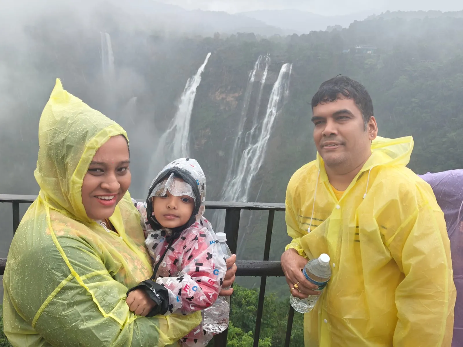 The family in rain ponchos at the Jog Falls viewpoint, the waterfalls in full flow through the rain.